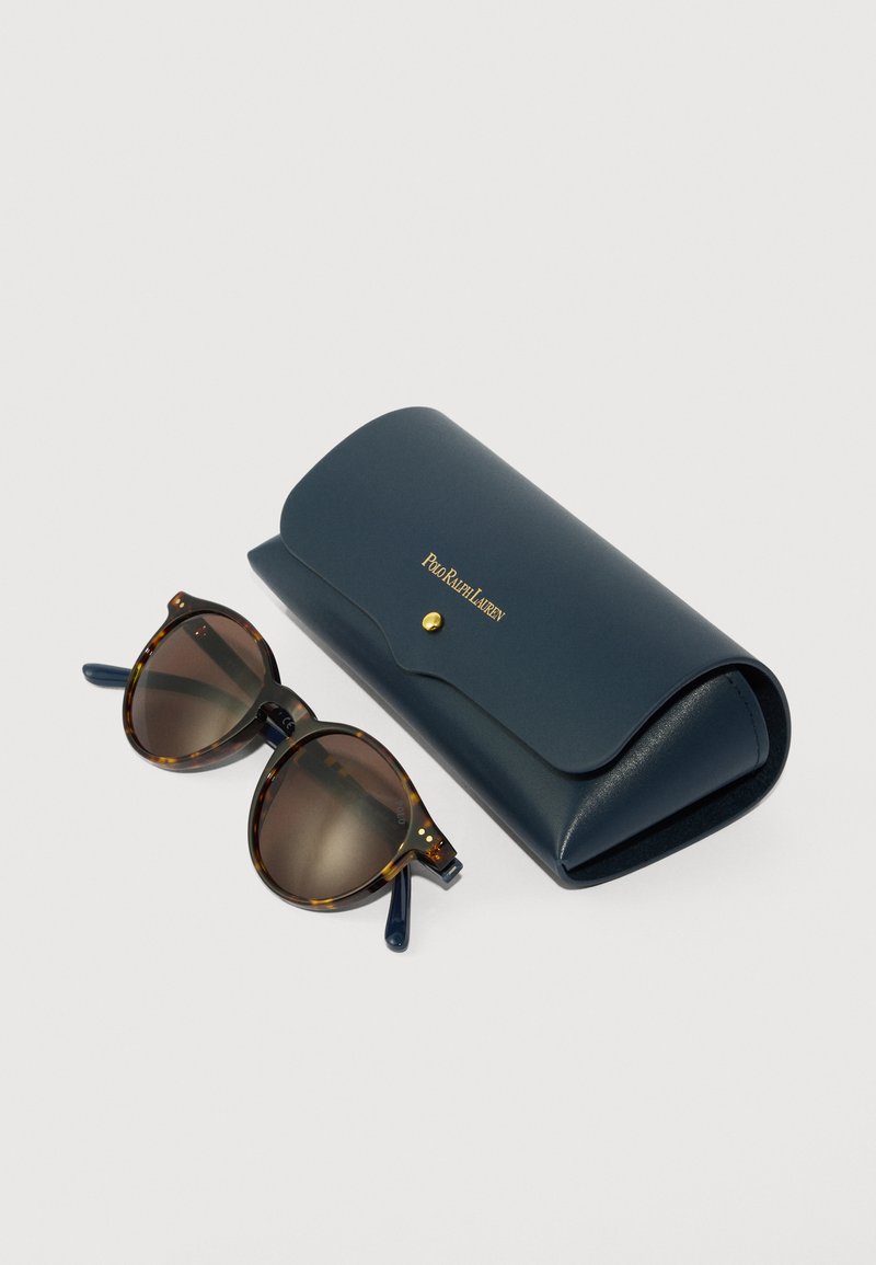 Tortoiseshell sunglasses with round brown lenses beside a navy blue Polo Ralph Lauren leather case with a gold snap button.