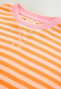 Gros plan d'un pull tricoté avec des rayures horizontales orange et beige et un col rond côtelé rose.