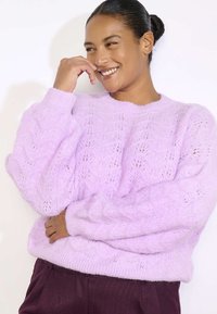 Svijetlopurple pleteni pulover s teksturiranim uzorkom, rebrastim izrezom i voluminoznim rukavima. Mekani, pahuljasti materijal pruža toplinu.