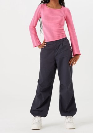 Top rosa a maniche lunghe e a coste con scollatura quadrata abbinato a pantaloni larghi blu scuro. Le sneakers bianche completano l'outfit.