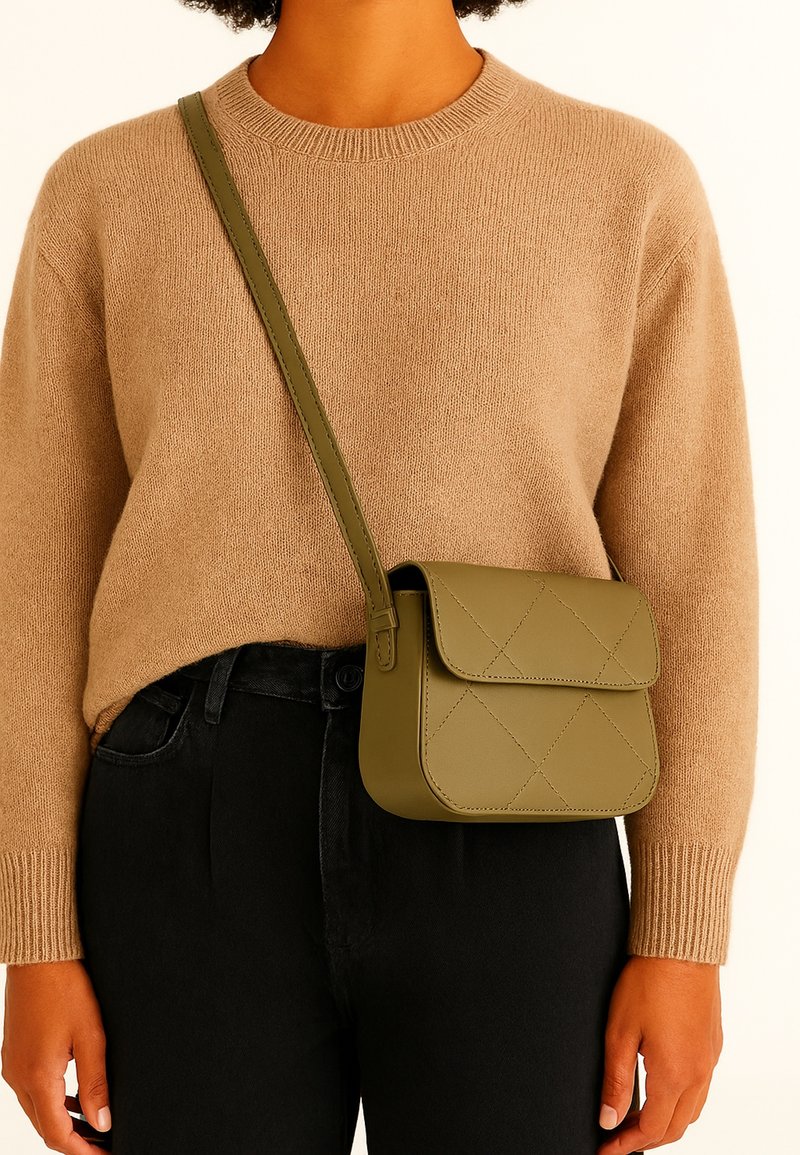 Olijfgroene, gewatteerde crossbodytas van soepel leer met een klep, contrasterend tegen een beige trui en zwarte jeans.