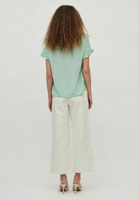 Blouse vert menthe à manches courtes avec une coupe décontractée ; associée à un pantalon crème à jambes larges. La tenue a une texture lisse et un détail minimal.