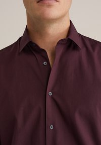 Bordo mygtukų marškiniai su klasikinėmis apykaklėmis, turintys tamsius mygtukus ir glotnų, lengvą audinį. Priartintas vaizdas prie apykaklės.