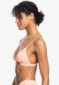 Perzikkleurige bikini-top met een driehoekig ontwerp, dunne verstelbare bandjes en een soepele textuur. Bevat een minimaal logo in het midden.
