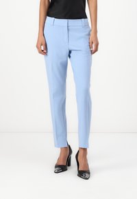 Light blue tailored pants with a flat front and slim fit, featuring side pockets and a smooth fabric texture. Worn with black heels.