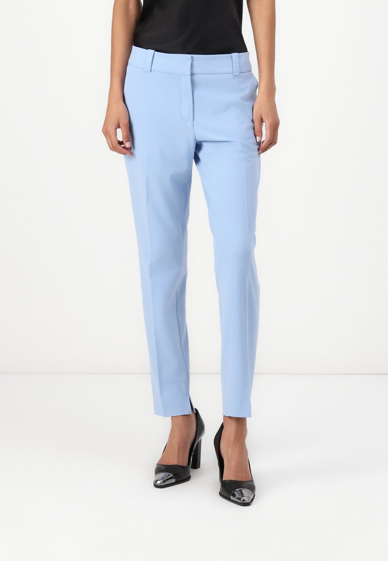 Light blue tailored pants with a flat front and slim fit, featuring side pockets and a smooth fabric texture. Worn with black heels.