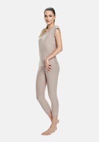 Top beige aderente con maniche corte abbinato a leggings coordinati. Entrambi realizzati in tessuto liscio e elastico. Design minimalista, finitura senza cuciture.