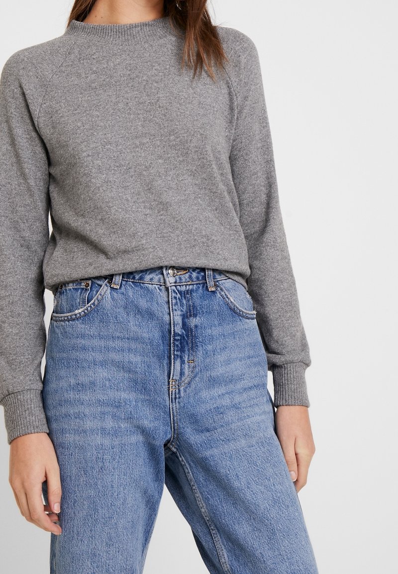 Szary sweter o splocie z ribbowymi mankietami, zestawiony z niebieskimi dżinsami o wysokim stanie z delikatnym wyblaknięciem i klasycznym pięciopocketowym fasonem.