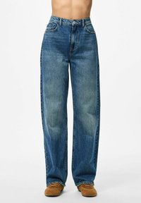 Široke plave traperice s izblijedjelim zavr�šetkom, visokim strukom, prednjim džepovima i šivanjem na rubu. Uparene s smeškim nubuk cipelama.