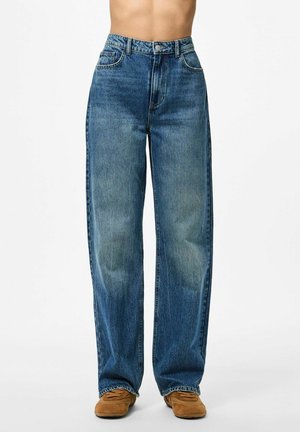 Breda blå denimbyxor med en blekt finish, hög midja, framfickor och en sydd fåll. Matchas med bruna mockaskor.