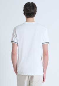 Camiseta blanca de manga corta con acentos en rayas grises en los puños, cuello redondo y una textura de tela suave y ligera.