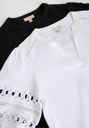 Hvide og sorte bluser med korte ærmer og blonde detaljer på ærmer og skuldre, V-hals og synlige mærker med teksten "Love & Roses".