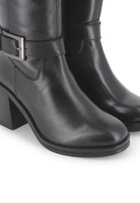 Botines de cuero negro con tacón cuadrado, que cuentan con un detalle de hebilla en el lateral y una textura suave. Diseño de punta redonda.