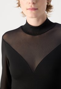 Top nero con collo alto e pannello in rete trasparente con design a V. Il tessuto ha una texture liscia e maniche aderenti.