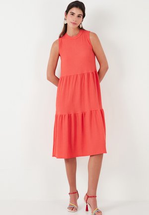 Coral sleeveless dress with a tiered design, lightweight textured fabric, knee-length cut, and a round neckline. Accented with strappy heels.