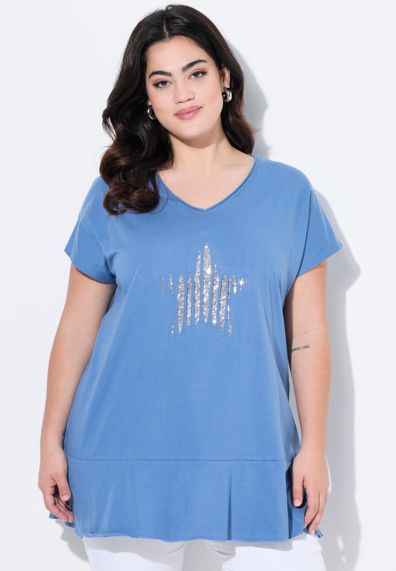 Camiseta de algodón azul con escote en V, mangas cortas y un dobladillo acampanado. Presenta un gráfico de estrella plateada en la parte delantera. Textura suave.