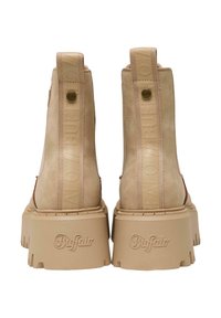 Botas de tobillo de ante beige con suela gruesa. Presenta un logo elevado en la parte trasera y una suela de goma texturizada para mayor agarre.