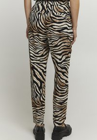 Broek met een zwart en crèmekleurig zebra patroon, met bruine accenten, elastische tailleband en zijzakken. Gemaakt van gemusterde stof.