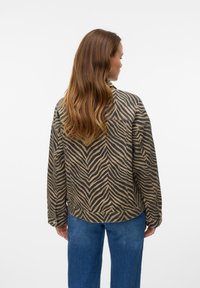 Prindikujuline jakk pruunides ja mustades toonides, mis on lõdva lõikega, ümarate äärtega ja nööpidega mansettidega, koos siniste teksapükstega.