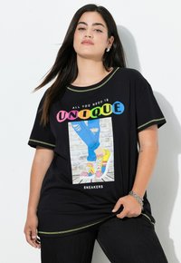 Sort t-shirt med farverig grafik, der står "ALT HVA DU BEHØVER ER UNIK", og med et design af slidte jeans og farverige sneakers nedenfor.