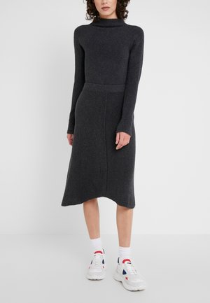Femme portant une robe en maille à manches longues gris foncé avec un col montant et des baskets blanches avec des accents rouges et bleus.