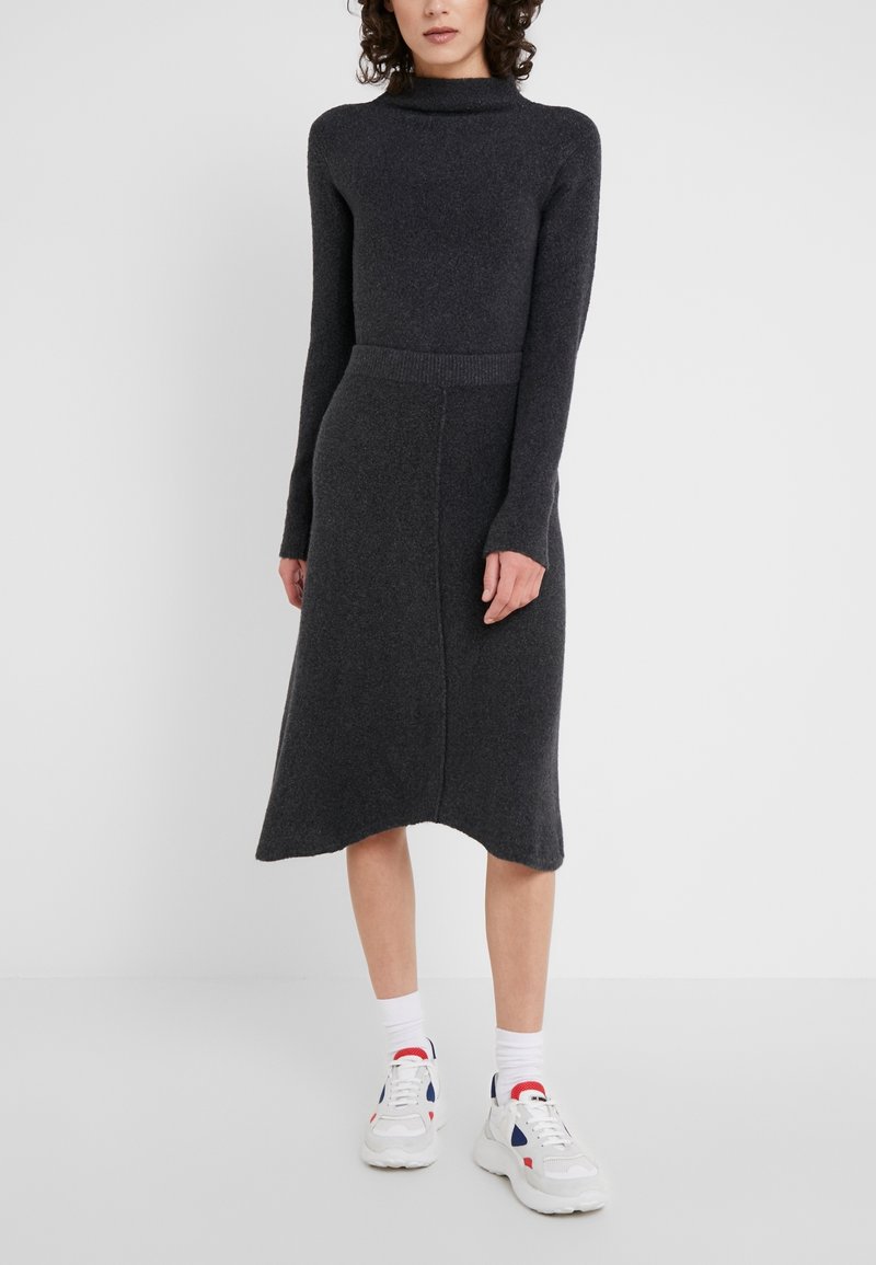 Mujer con un vestido de punto gris oscuro de manga larga y cuello alto, y zapatillas blancas con detalles en rojo y azul.