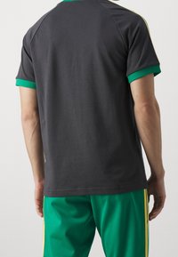 Grå atletisk t-shirt med grön ribbad krage och ärmslut, med en mjuk textur och korta ärmar. Kombinerad med gröna byxor med gula ränder.