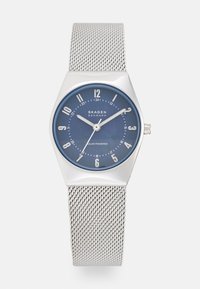 Srebrny zegarek na siateczkowym pasku z sześciokątną kopertą, niebieską tarczą, białymi znacznikami godzin oraz wskazówkami. Posiada napęd solarny i wypolerowane wykończenie.