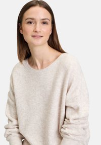Helles beiges, weiches Strickoberteil mit weit ausgeschnittenem Hals und leicht übergroßen Ärmeln, das ein dezentes strukturiertes Muster aufweist.