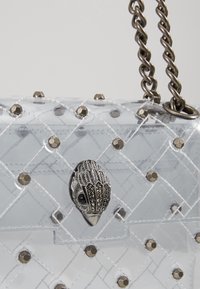 Borsa trasparente in plastica con motivo a quilt, hardware argentato e dettagli decorativi. Presenta una tracolla a catena e un design di chiusura unico.