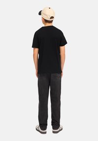Camiseta de algodón negra, pantalones de mezclilla grises, gorra beige. Corte recto. La vista trasera muestra un diseño simple, sin patrones ni acentos visibles.