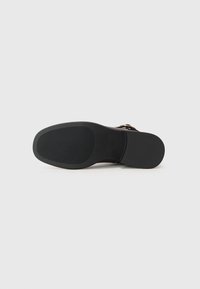 Suela de zapato de goma negra con textura acanalada y forma redondeada; presenta un borde liso y un ligero tacón, sin marcas visibles ni detalles adicionales.