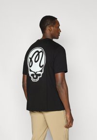 Μαύρο βαμβακερό T-shirt με μεγάλο λευκό γραφικό κρανίο με περίπλοκο σχέδιο στην πλάτη. Λαιμόκοψη crew, κοντά μανίκια, άνετη εφαρμογή.