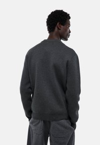 Sweater gris foncé avec un col rond, des poignets et un ourlet côtelés, présentant une texture lisse et un design minimaliste. Vu de l'arrière.