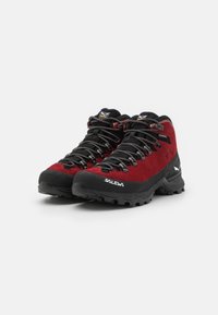 Røde moccasiner for fotturer med sorte gummisåler, med høy ankeldesign, tykke lisser og fremtredende merkevare på siden.