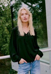Schwarzes Langarmoberteil mit V-Ausschnitt und Knopfdetails, kombiniert mit hellblauen Jeans. Weicher Stoff mit weiten Ärmeln.