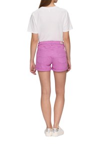 Shorts en denim rose avec des revers, deux poches arrière et une taille standard, associés à un t-shirt blanc uni et des baskets argentées.