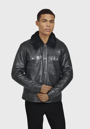 Chaqueta de cuero negro con cuello de pelaje sintético, botones frontales y dos bolsillos en el pecho. Presenta una textura suave y un diseño ajustado.