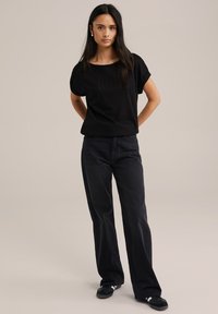 Mustaga tekstuuriga lühikeste varrukatega topp, mis on vabalt istuv, koos kõrge vöökohaga mustade laiade pükstega. Riietus sisaldab musti jalanõusid.