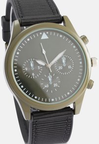 Ελιά πράσινο ρολόι με στρογγυλή πρόσοψη, μαύρο υφασμάτινο λουράκι, τρία υπο-ρολόγια, ασημί λεπτομέρειες και μίνιμαλ σχεδίαση.