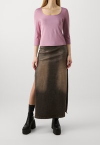 Pitkä tummanruskea hame, jossa on kevyt kiilto, sivuventtiili, yhdistettynä tiukkaan vaaleanpunaisiin kolme neljänneksen hihoihin ja mustiin korkokenkiin.