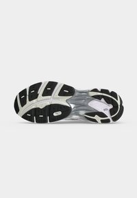Semelle d'une chaussure de course avec des motifs de bande de roulement noir et blanc et un amorti en gel visible au niveau du talon sur fond blanc.