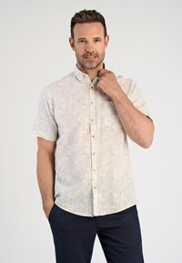Camicia a maniche corte con bottoni in beige chiaro con un motivo floreale sottile, dotata di taschino frontale e orlo rotondo, abbinata a pantaloni navy.