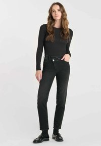 Jean en denim noir taille haute avec une coupe droite et fermeture à bouton, associés à un haut noir ajusté à manches longues et des mocassins noirs.