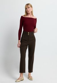 Top burdeos de canalé sin mangas con mangas largas, combinado con pantalones marrones de cintura alta que cuentan con tres botones dorados y un ajuste entallado.