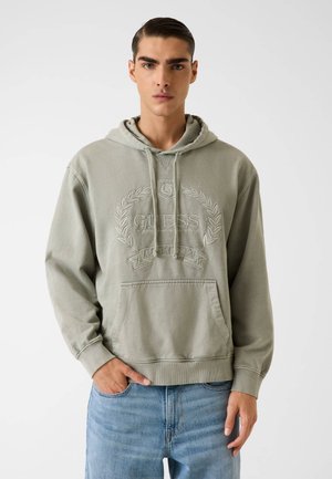 Hellgrüner Hoodie mit einer Fronttasche, ausgestattet mit dem geprägt "GUESS" Logo und Lorbeerdesign. Hergestellt aus weichem Stoff mit Kapuze und Kordelzug.