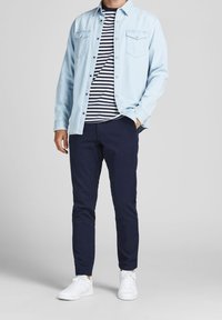 Ljusblå denimskjorta med knappar ovanpå en svartvit randig t-shirt, tillsammans med marinblå byxor och vita sneakers.