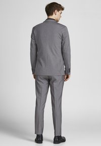 Veste de costume grise avec une coupe ajustée, texture unie, revers crantés et deux boutons. Assortie avec un pantalon gris et des chaussures noires.