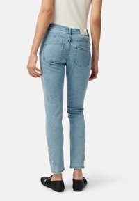 Jasnoniebieskie dżinsy o dopasowanym kroju, z tylnymi kieszeniami i haftowanymi akcentami na dolnej krawędzi. Noszone z czarnymi płaskimi butami.