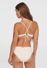 Biely bikiny set s nastaviteľnými popruhmi, prekríženým chrbtom a viazaním. Hladká tkanina s minimálnymi hardvérovými akcentmi.